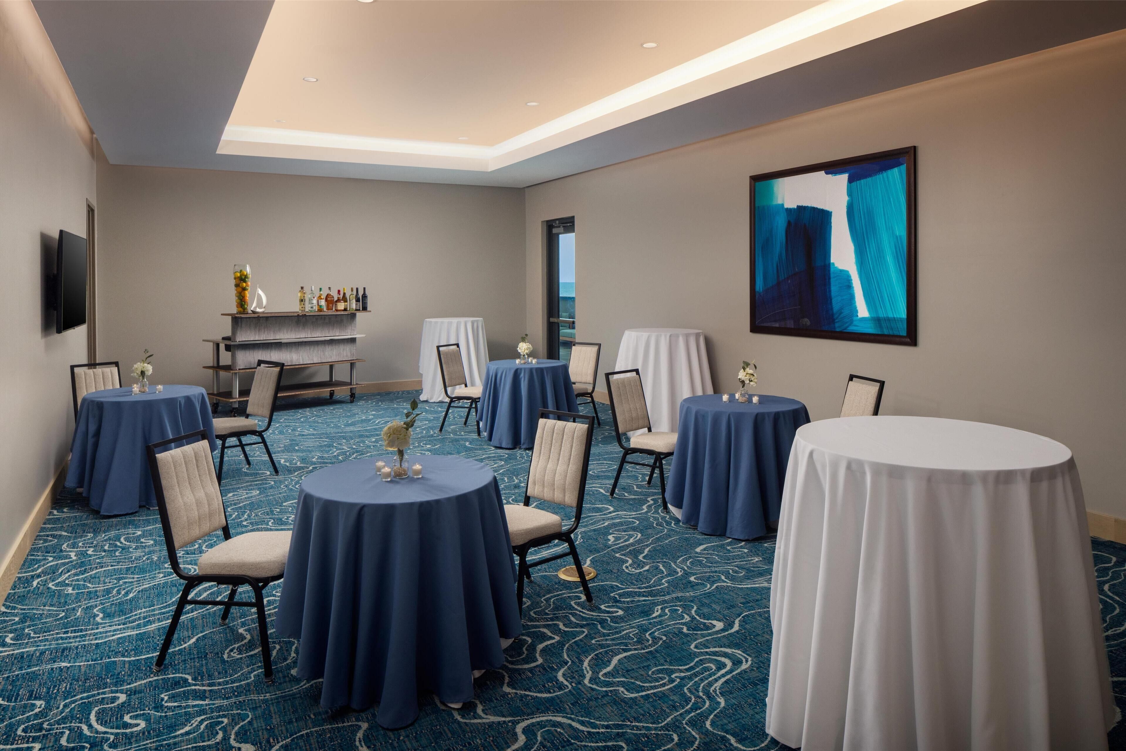 A conference room with round tables, chairs, a bar area, and a large abstract painting on the wall.