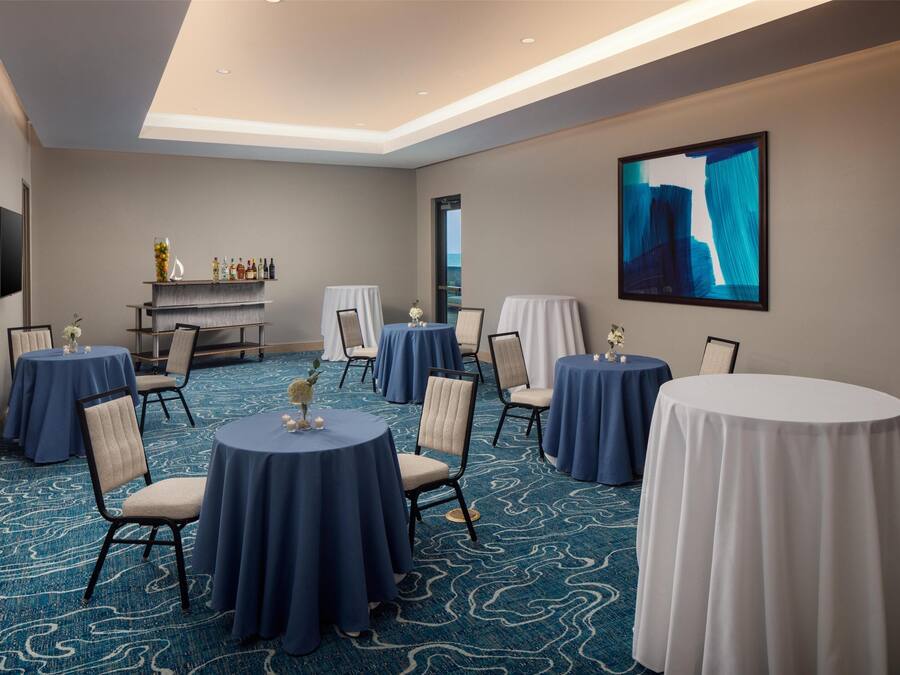 A conference room with round tables, chairs, a bar area, and a large abstract painting on the wall.