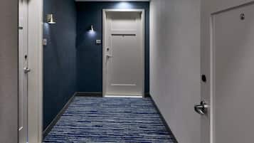 A hallway with a blue carpet, a white door, and a wall-mounted light fixture.