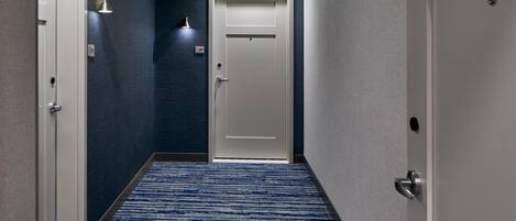 Un pasillo con alfombra azul, una puerta blanca y una lámpara fijada a la pared.