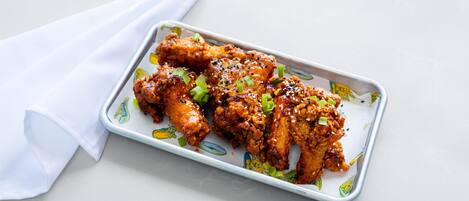 A tray of chicken wings garnished with sesame seeds and green onions, placed on a white surface with a white napkin beside it.