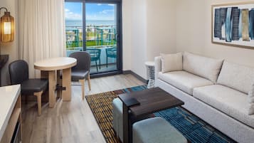 A modern hotel room with a balcony, a dining area, a sofa, and a coffee table.