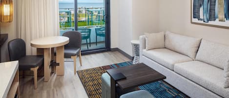 A modern hotel room with a balcony, a dining area, a sofa, and a coffee table.