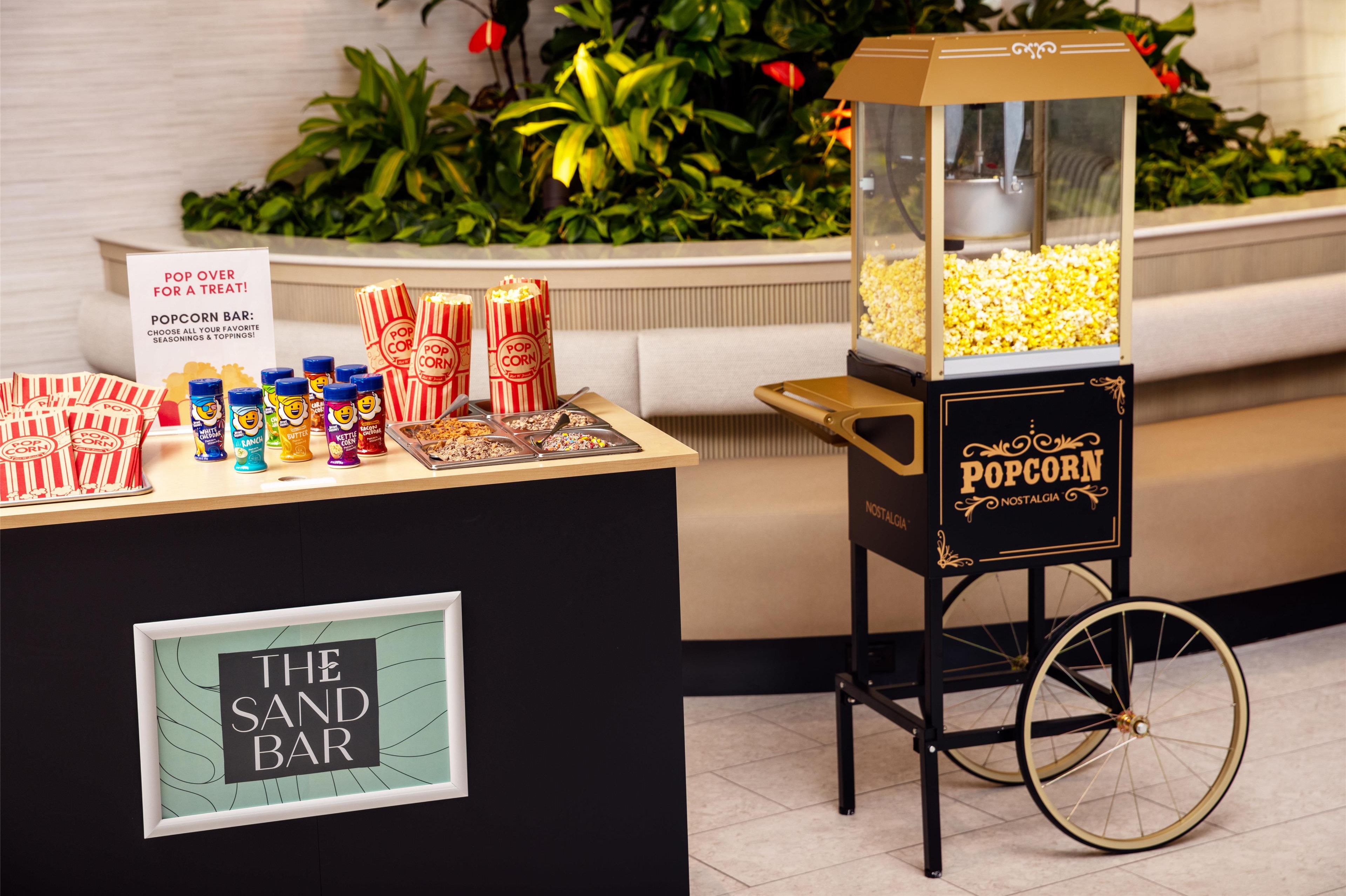 Een popcornkraam met een klassieke kar, voorzien van de tekst 'Nostalgia', en een bord waarop staat 'Kom langs voor een lekkernij!'.