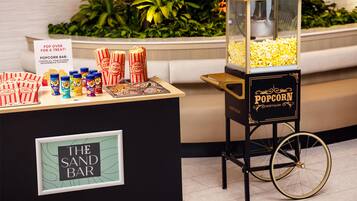A popcorn bar with a vintage cart, labeled 'Nostalgia', and a sign reading 'Pop Over for a Treat!'.