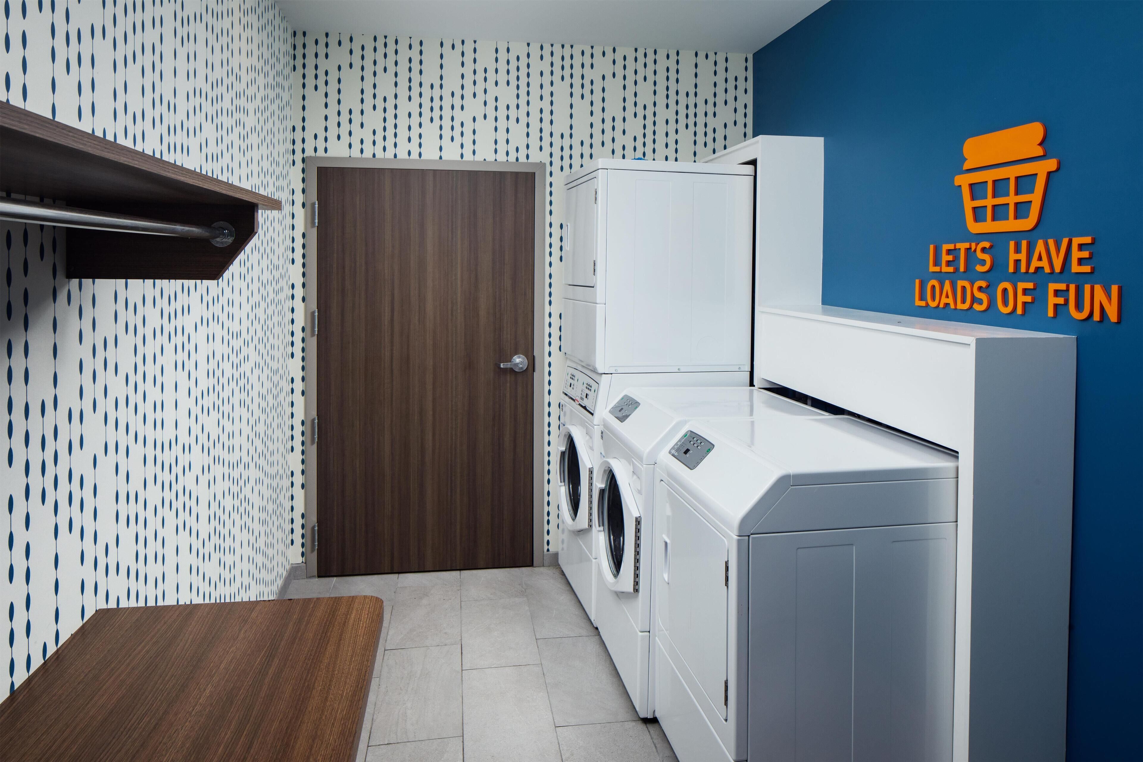 A laundry room with a washing machine and dryer, a wooden door, and a blue wall with a pattern.