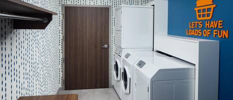 A laundry room with a washing machine and dryer, a wooden door, and a blue wall with a pattern.