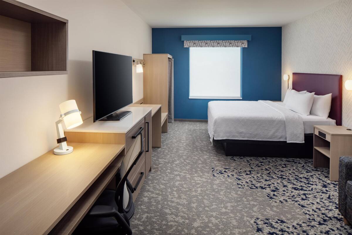 Habitación de hotel con cama, escritorio con televisor, silla, armario y ventana con vistas.