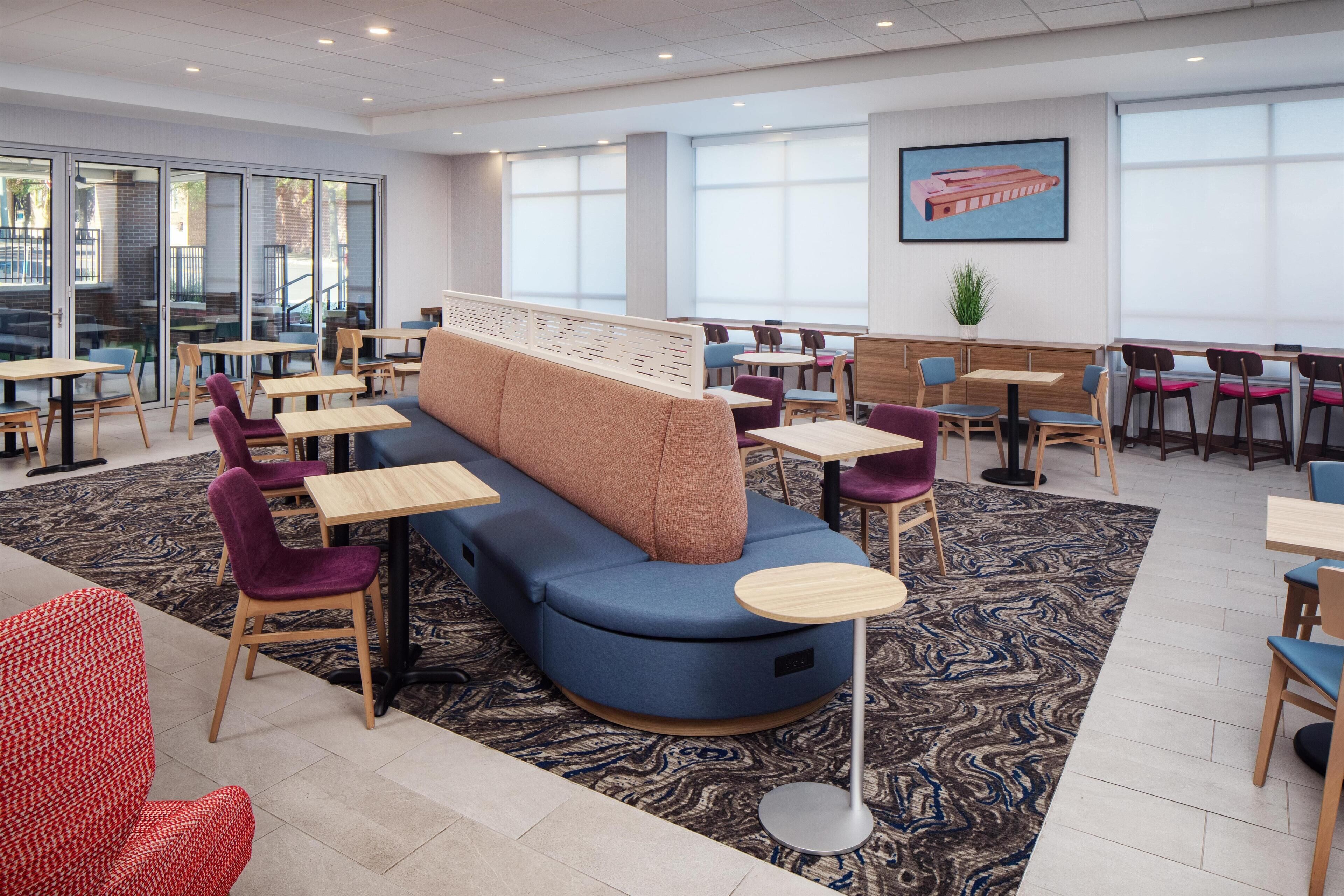 Un espace repas moderne avec un canapé bleu, des tables en bois et des chaises violettes.