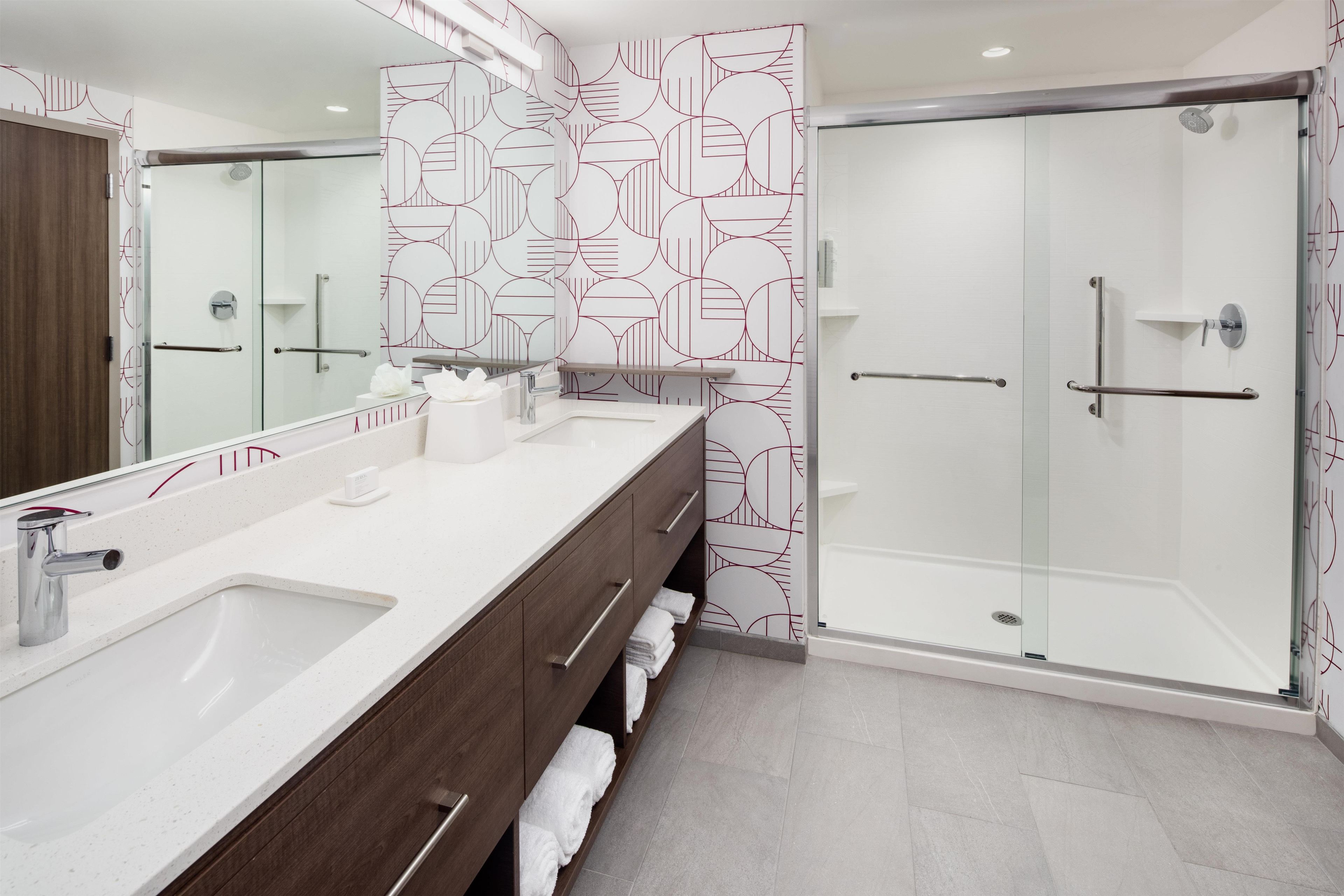 Un baño moderno con un espejo grande, dos lavamanos, una ducha y un perchero para toallas.