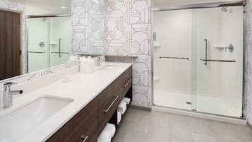 Un baño moderno con un espejo grande, dos lavamanos, una ducha y un perchero para toallas.