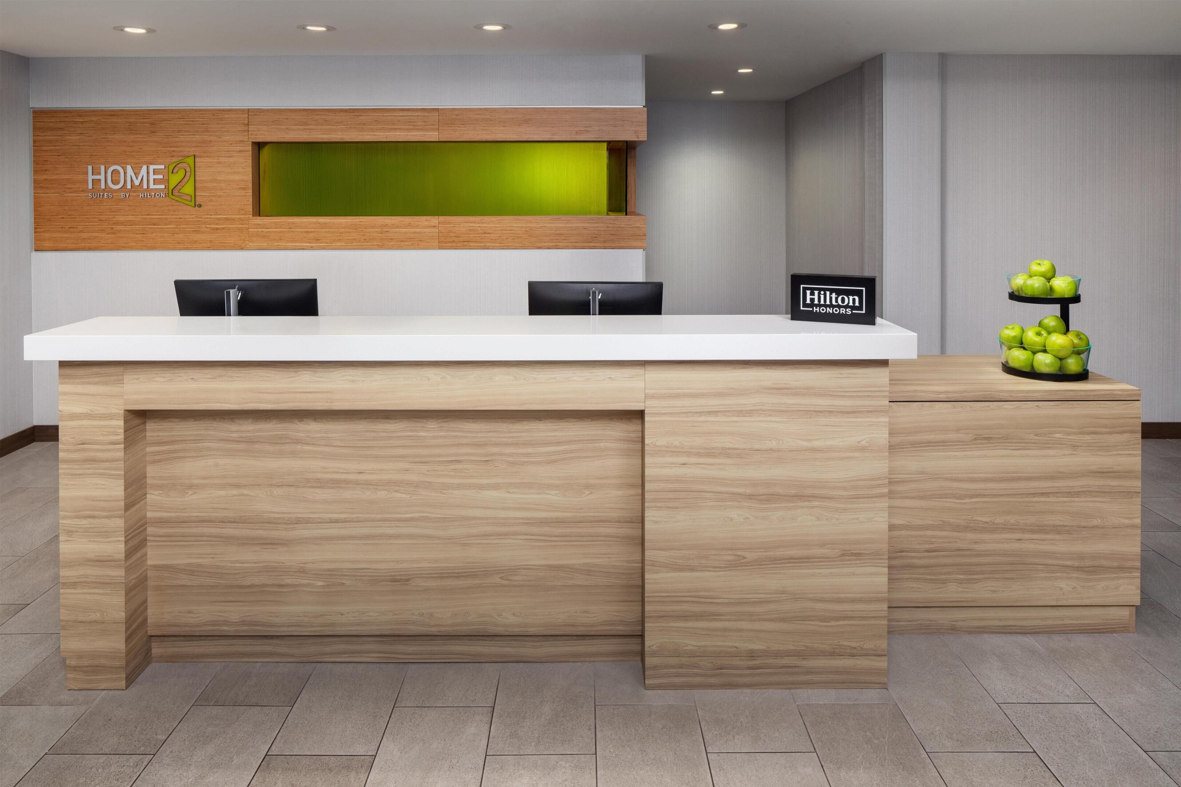 A hotel reception desk with a wooden finish, a green accent wall, and a sign indicating 'Hilton'.