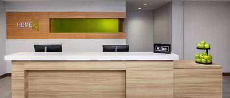 A hotel reception desk with a wooden finish, a green accent wall, and a sign indicating 'Hilton'.