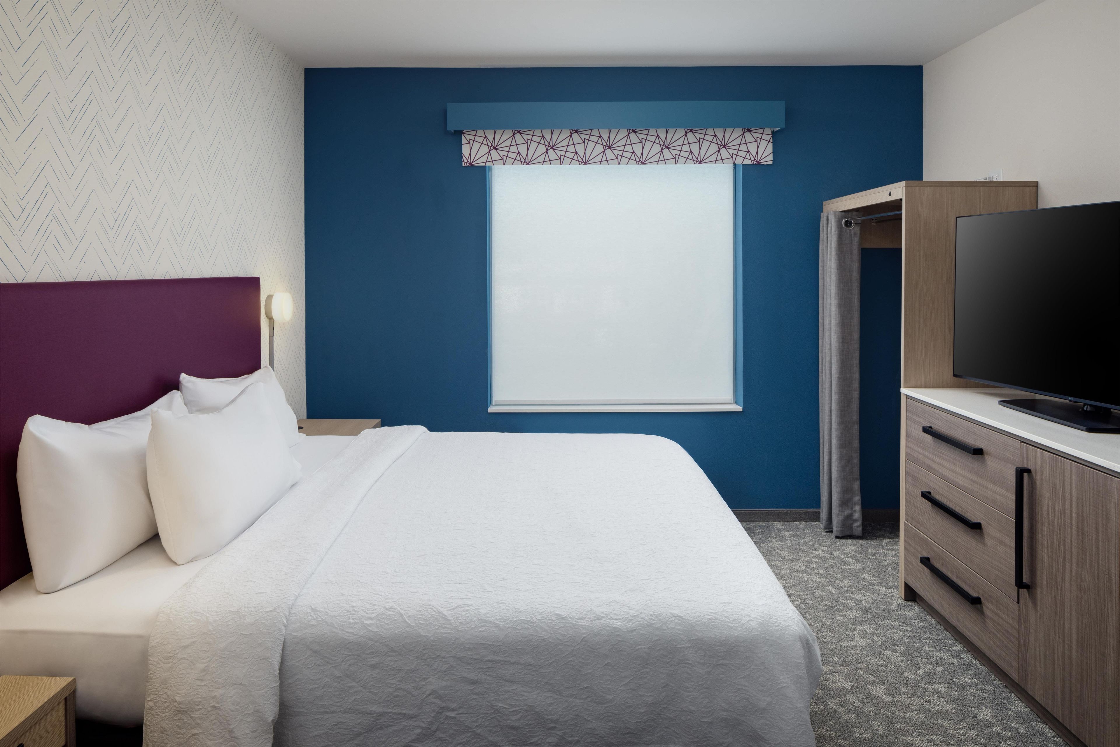 Habitació d'hotel amb un llit, una televisió, un armari i una finestra amb cortina estampada.