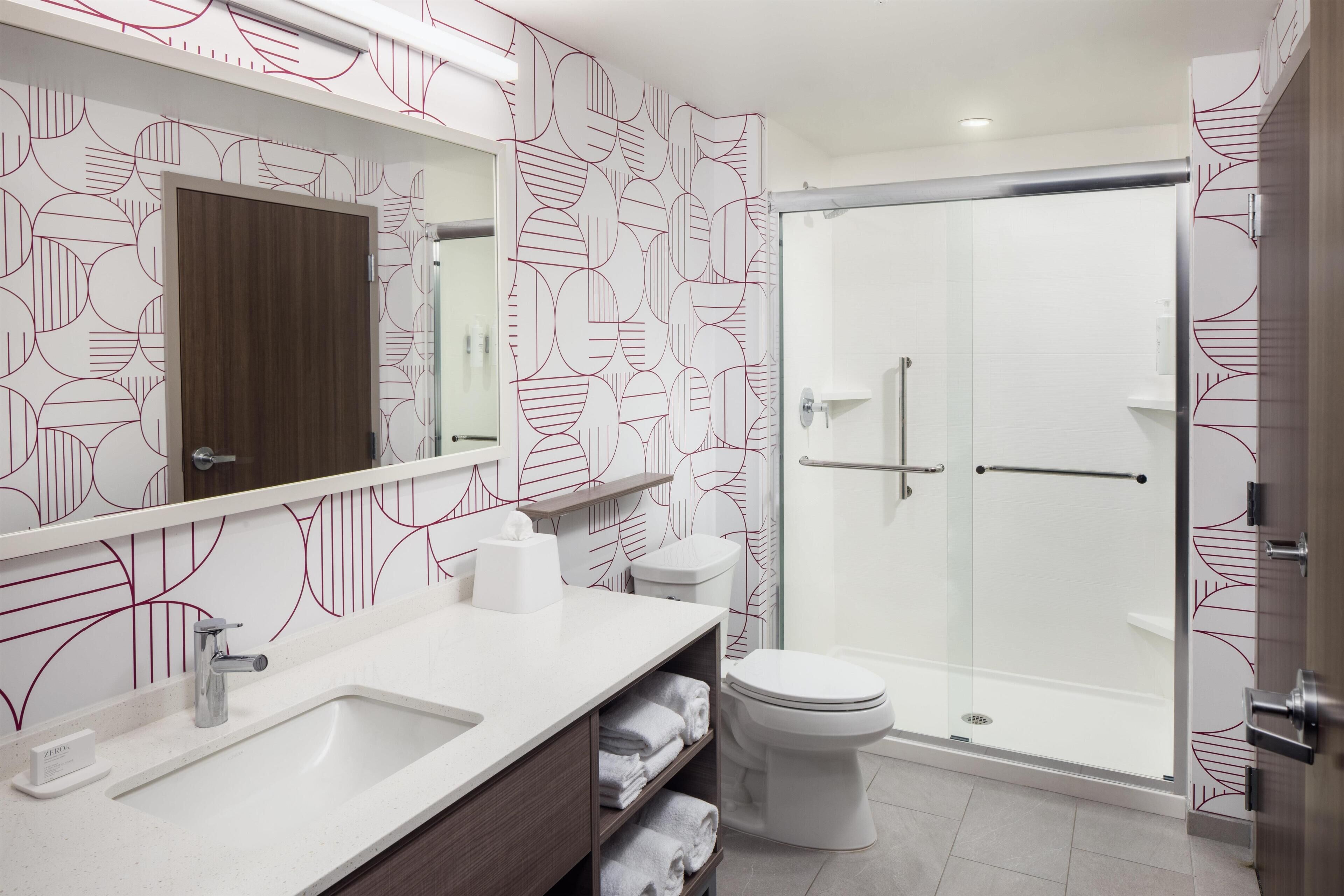 A modern bathroom with a large mirror, a sink, a toilet, and a glass-enclosed shower.