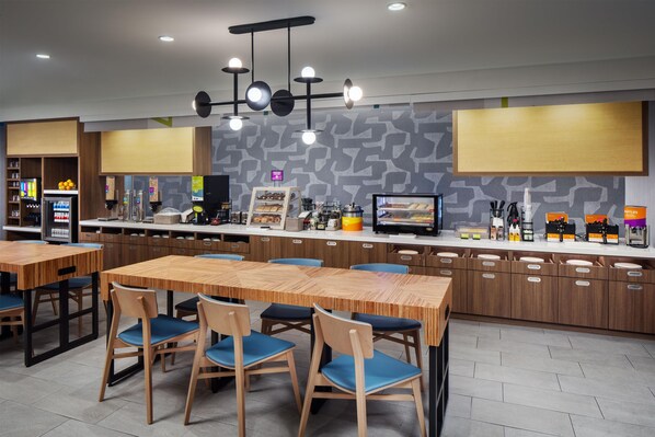 A modern cafe with wooden tables and chairs, a coffee machine, and a display case with pastries. - Home2 Suites By Hilton Memphis Downtown (Memphis)