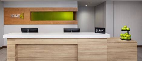 Bancada de recepção de hotel com acabamento em madeira, parede de destaque verde e placa indicando 'Hilton Honors'.