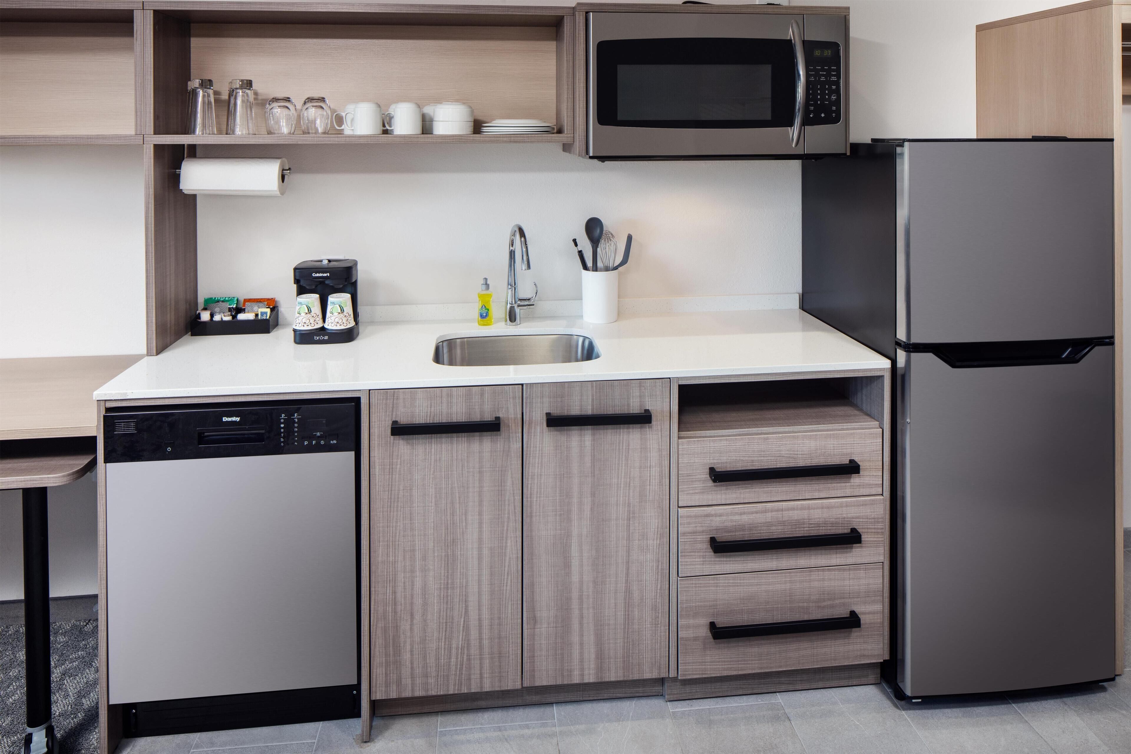 A modern kitchen with a dishwasher, microwave, refrigerator, and wooden cabinets.