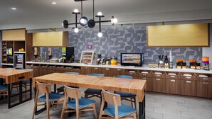 Un restaurante moderno con mesas de madera y sillas azules, una barra con mostradores de comida y una pared con diseño.
