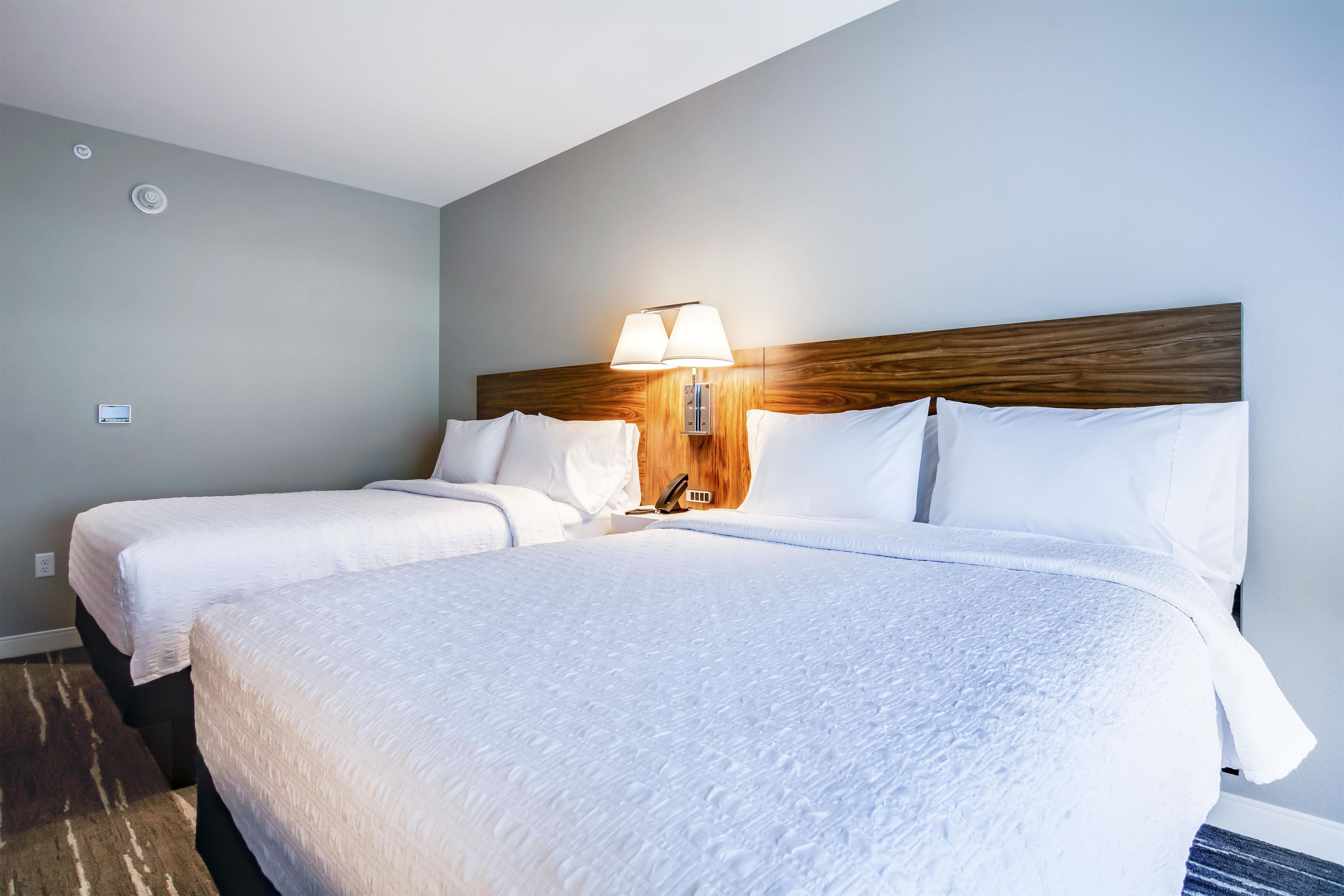 A hotel room with two beds, a wooden headboard, a bedside lamp, and a wall-mounted thermostat.