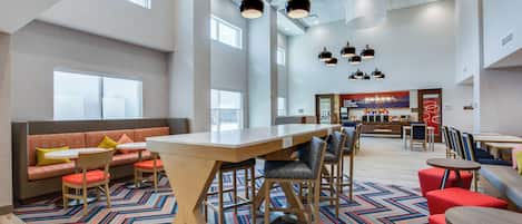 A spacious lobby with a long wooden table, multiple seating areas, and a patterned carpet.