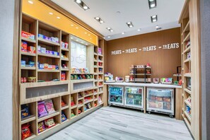 A well-organized snack and treat section with multiple shelves stocked with various products, a refrigerated display case, and a wall sign indicating the section. - Hampton Inn & Suites By Hilton Louisville East Oxmoor (Louisville)