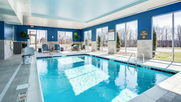 An indoor swimming pool with clear blue water, surrounded by large windows offering a view of the outdoors. - Hampton Inn & Suites By Hilton Louisville East Oxmoor (Louisville)