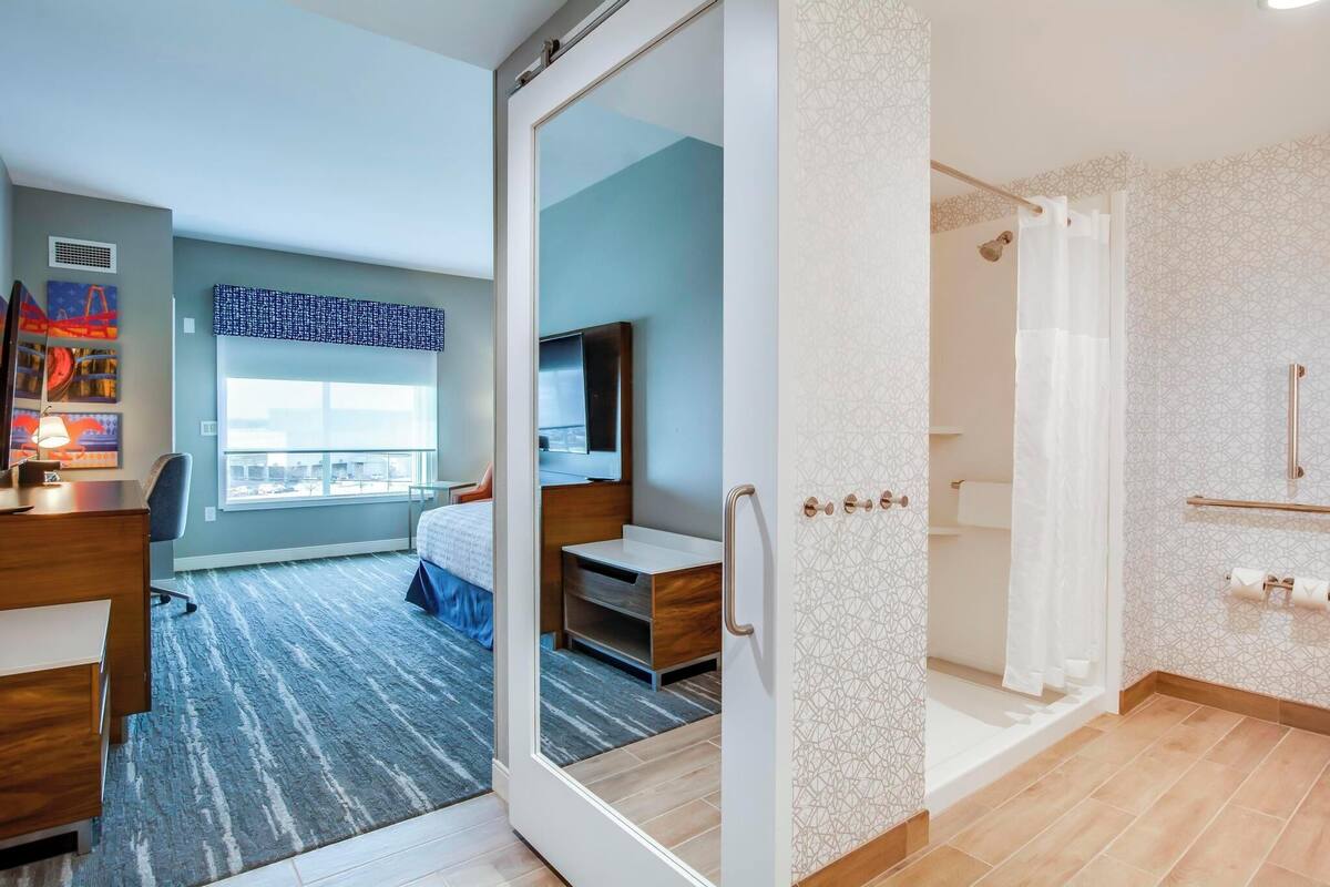 Una habitación de hotel moderna con una cama grande, un escritorio, un televisor y una ducha.