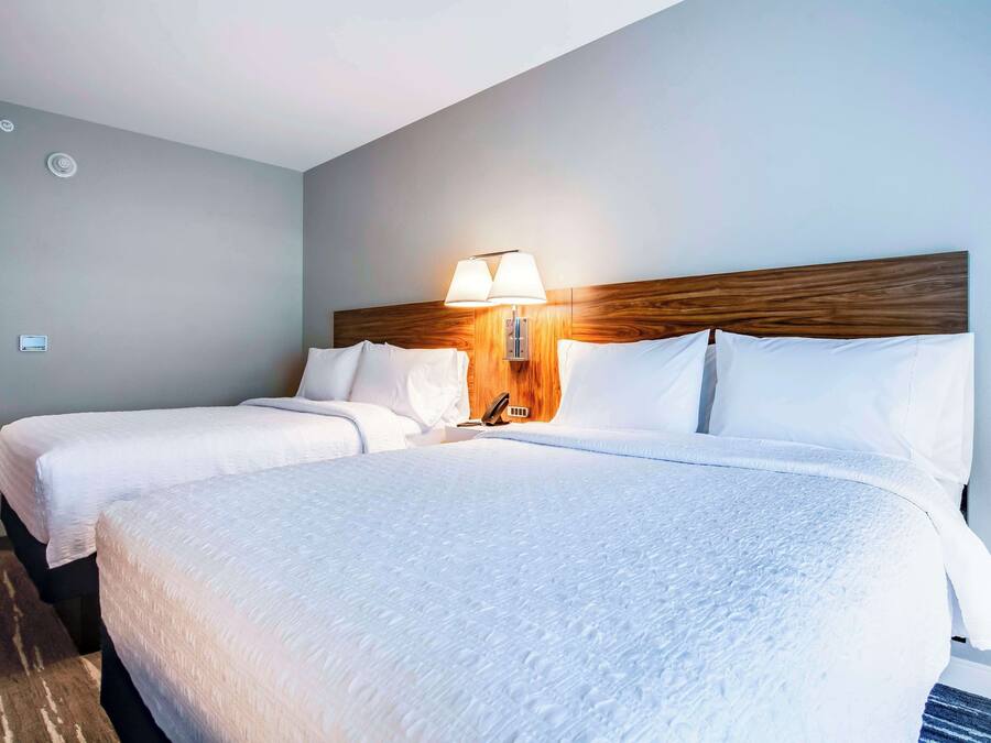 Ein Hotelzimmer mit zwei Betten, einem hölzernen Kopfteil, einer Wandlampe und einem Teppichboden.