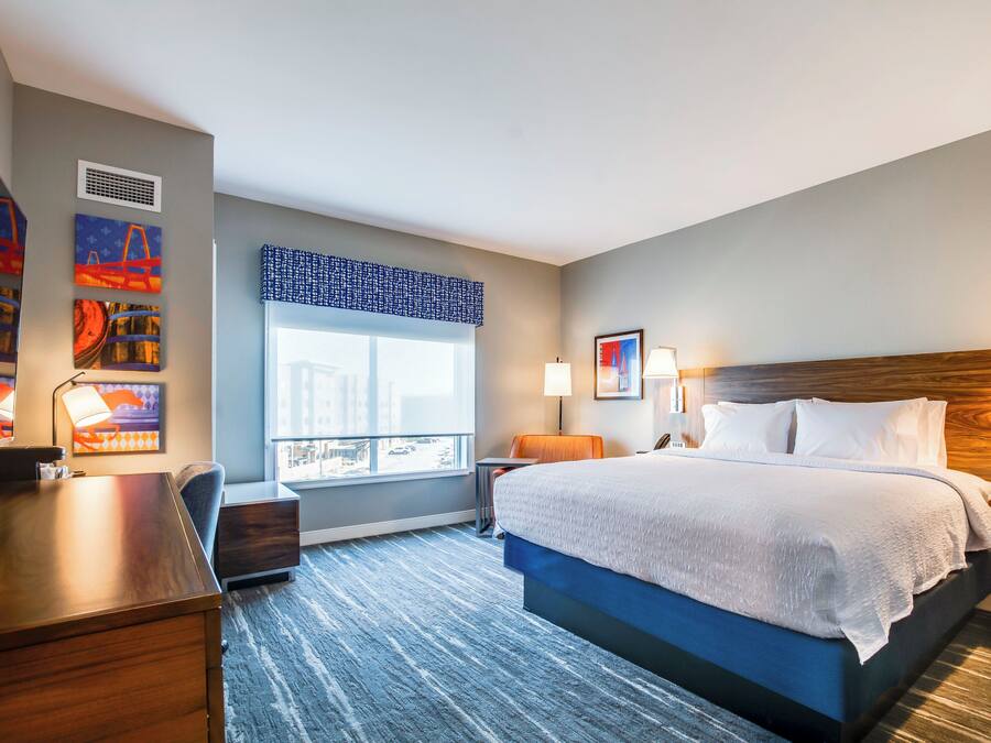Ein Hotelzimmer mit einem großen Bett, einem Schreibtisch, einem Sessel, einem Fenster mit Aussicht und Bildern an den Wänden.