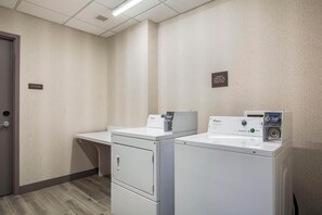 Une buanderie équipée de deux machines à laver et deux sèche-linge à chargement frontal, d’un espace de rangement et d’un panneau indiquant l’emplacement.
