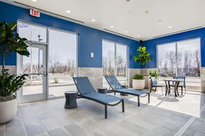 A modern indoor area with a blue wall, large windows, and a seating area with chairs and tables. - Hampton Inn & Suites By Hilton Louisville East Oxmoor (Louisville)
