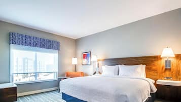 A hotel room with a large bed, two bedside tables with lamps, a window with a view of buildings, and a wooden headboard.