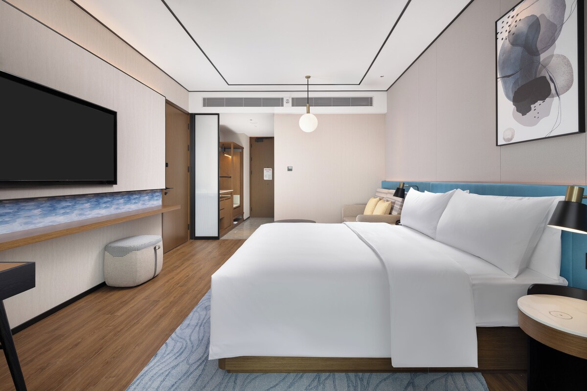 A modern hotel room with a bed, a flat-screen TV, a desk, and a wall-mounted artwork.