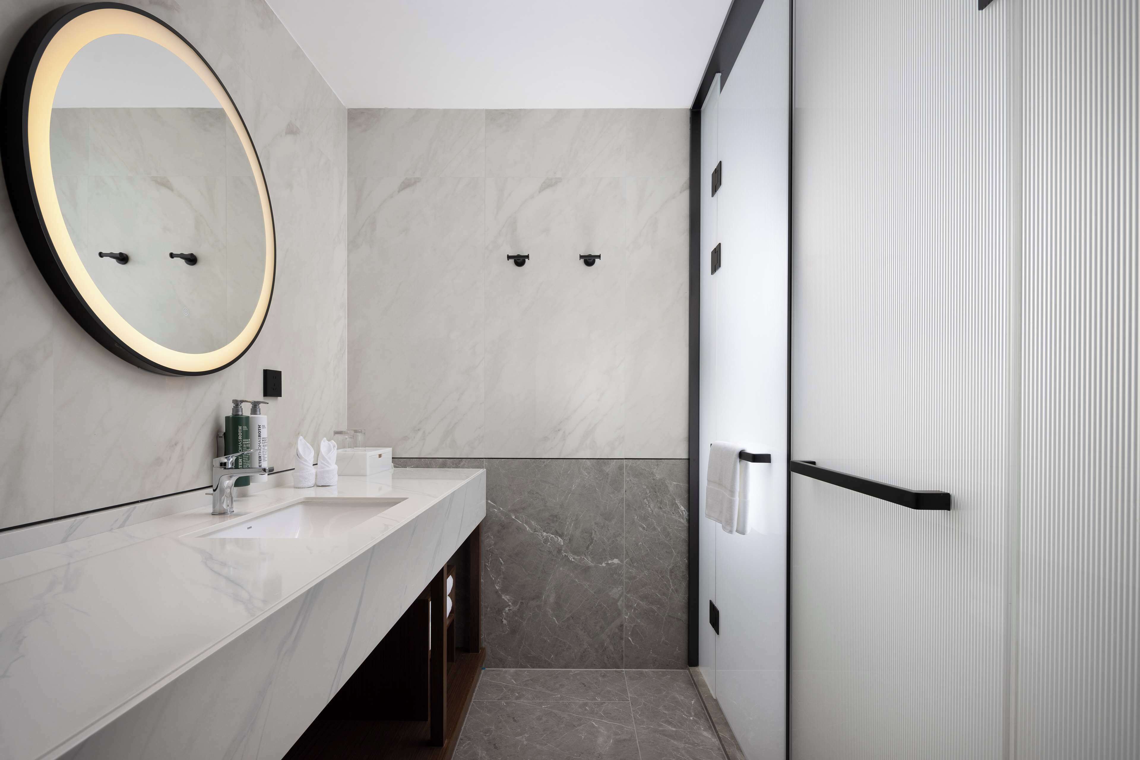 A modern bathroom with a marble vanity, a large mirror, and a walk-in shower.