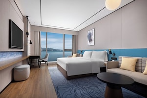 Habitación de hotel moderna con una cama grande, un sofá, un televisor y vistas al agua.