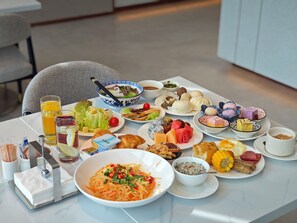 A table set with a variety of dishes including noodles, dumplings, and fruits, along with beverages and condiments. - Hilton Garden Inn Shanwei Haibin Boulevard (Shanwei)