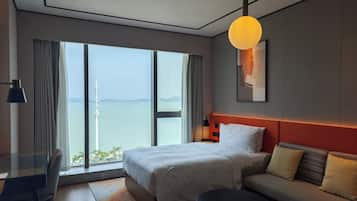Habitación de hotel moderna con una cama grande, un sofá, una mesa redonda y vistas al mar.