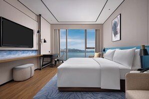 A modern hotel room with a large bed, a desk, a television, and a view of a body of water. - Hilton Garden Inn Shanwei Haibin Boulevard (Shanwei)