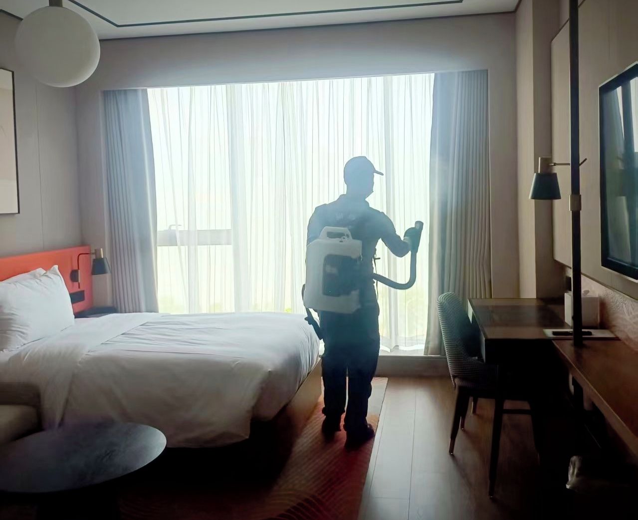 A hotel room with a bed, a desk, a chair, a TV, and a large window with curtains.