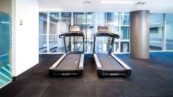 Two stationary treadmills in a modern indoor space with large windows and a visible staircase in the background.