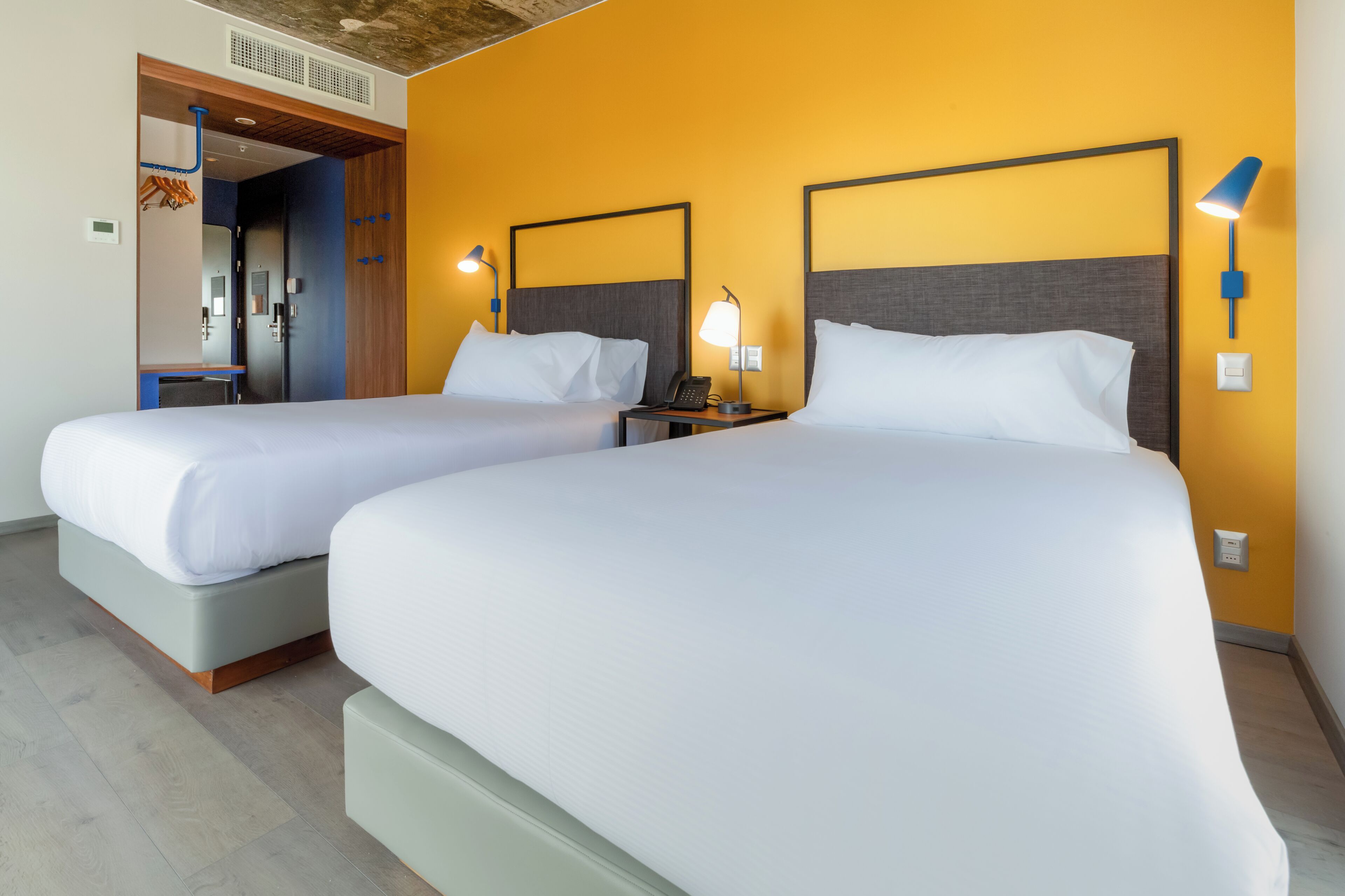 A hotel room with two beds, a wooden ceiling, and a yellow wall.