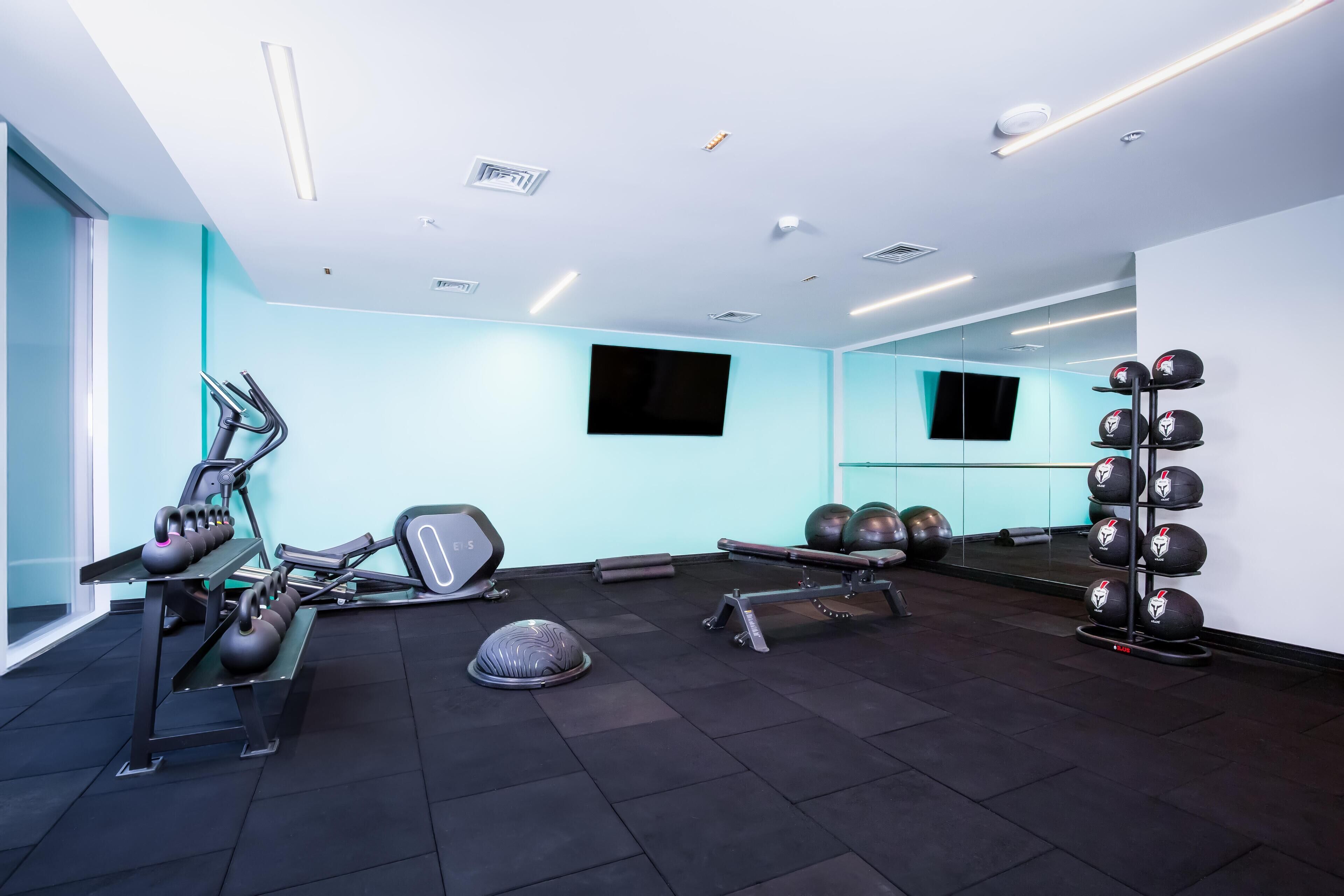 A modern gym with exercise equipment, a mirrored wall, and a black floor.