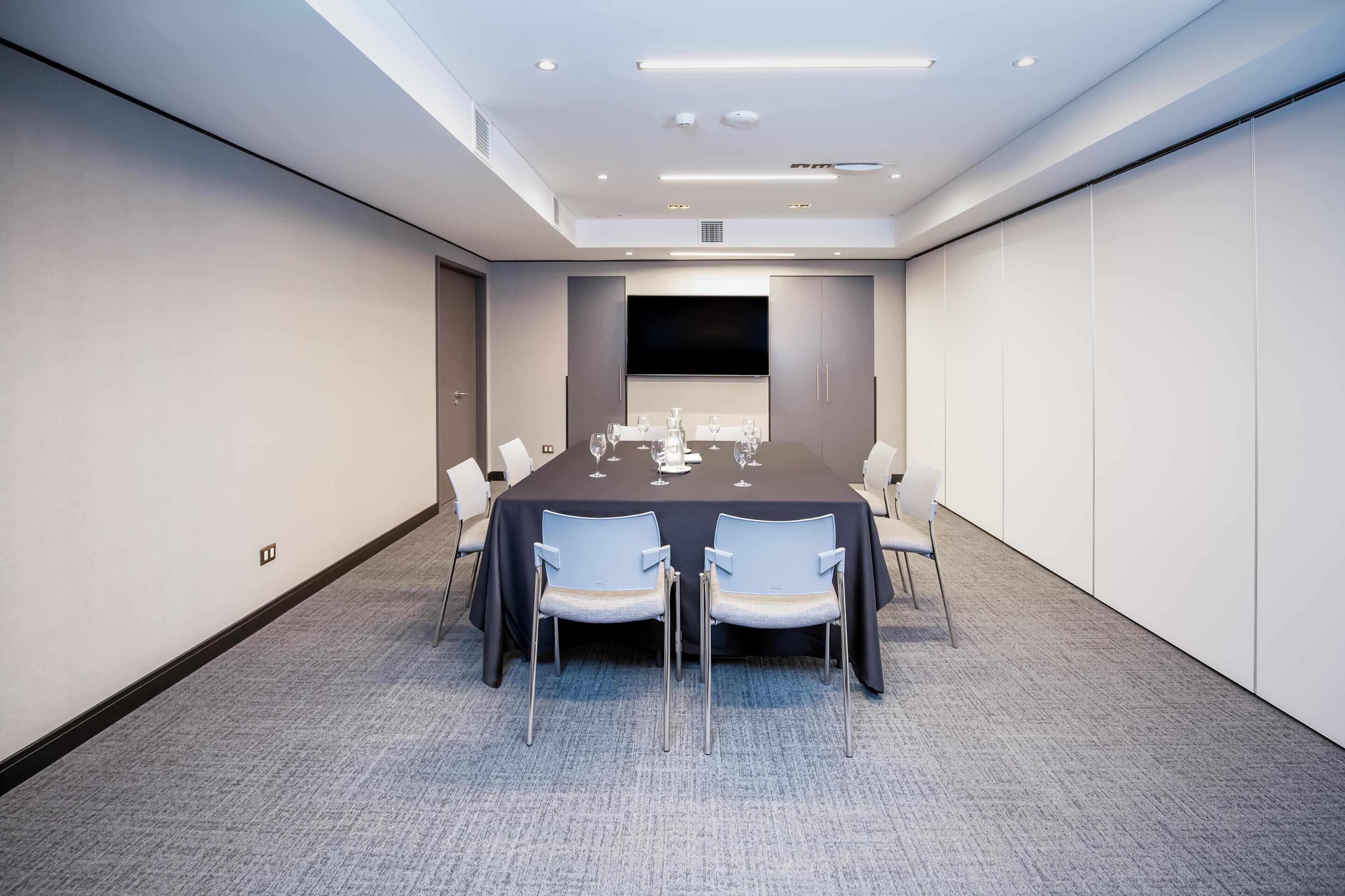 A conference room with a long table, chairs, and a flat-screen TV.
