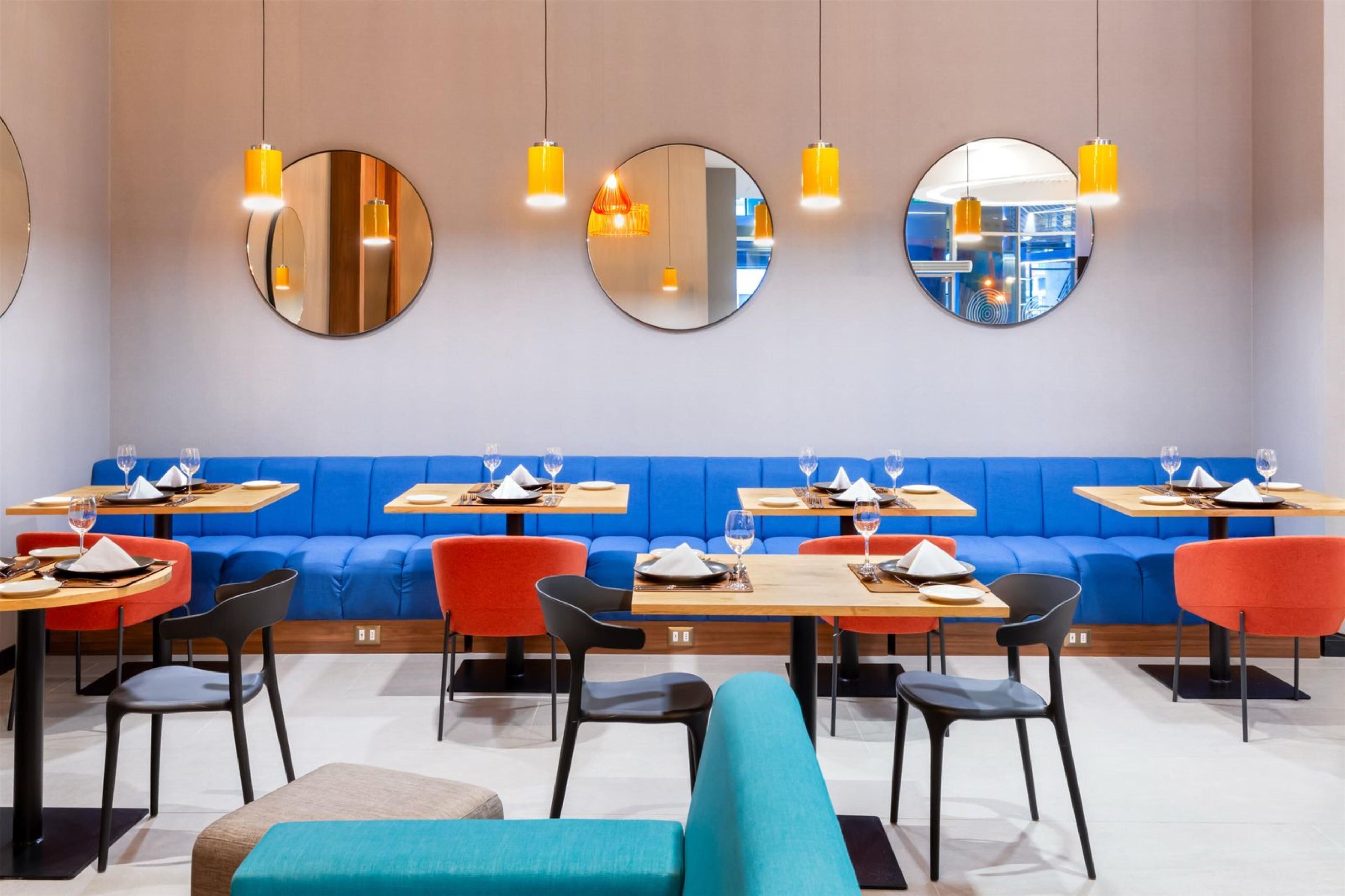 Un restaurante moderno con espejos redondos en la pared, asientos azules y anaranjados y mesas de madera.