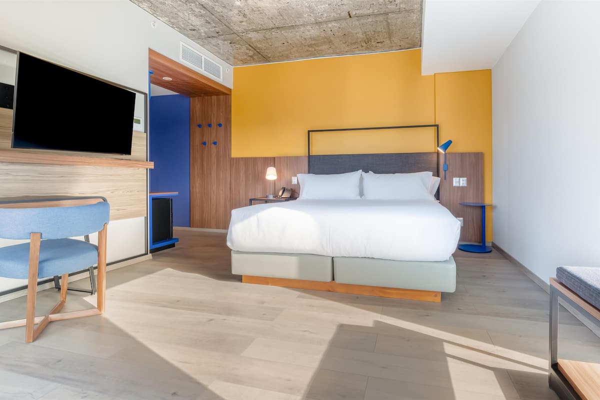 A modern hotel room with a bed, a desk, a chair, and a TV.