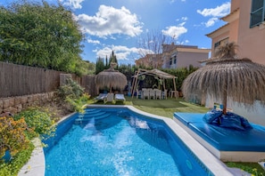A swimming pool with a pergola and lounge chairs, surrounded by greenery and a stone wall.