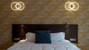 Un lit avec une literie blanche, une tête de lit sombre et deux appliques murales dotées d’abat-jours circulaires.