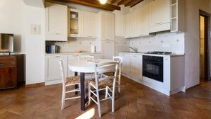 A kitchen with white cabinets, a dining table with chairs, a stove, and a television on a wooden cabinet.