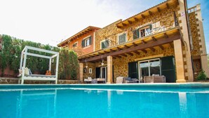 Un espace aménagé au bord de la piscine, avec un bâtiment en pierre, du mobilier d’extérieur et un coin salon abrité.